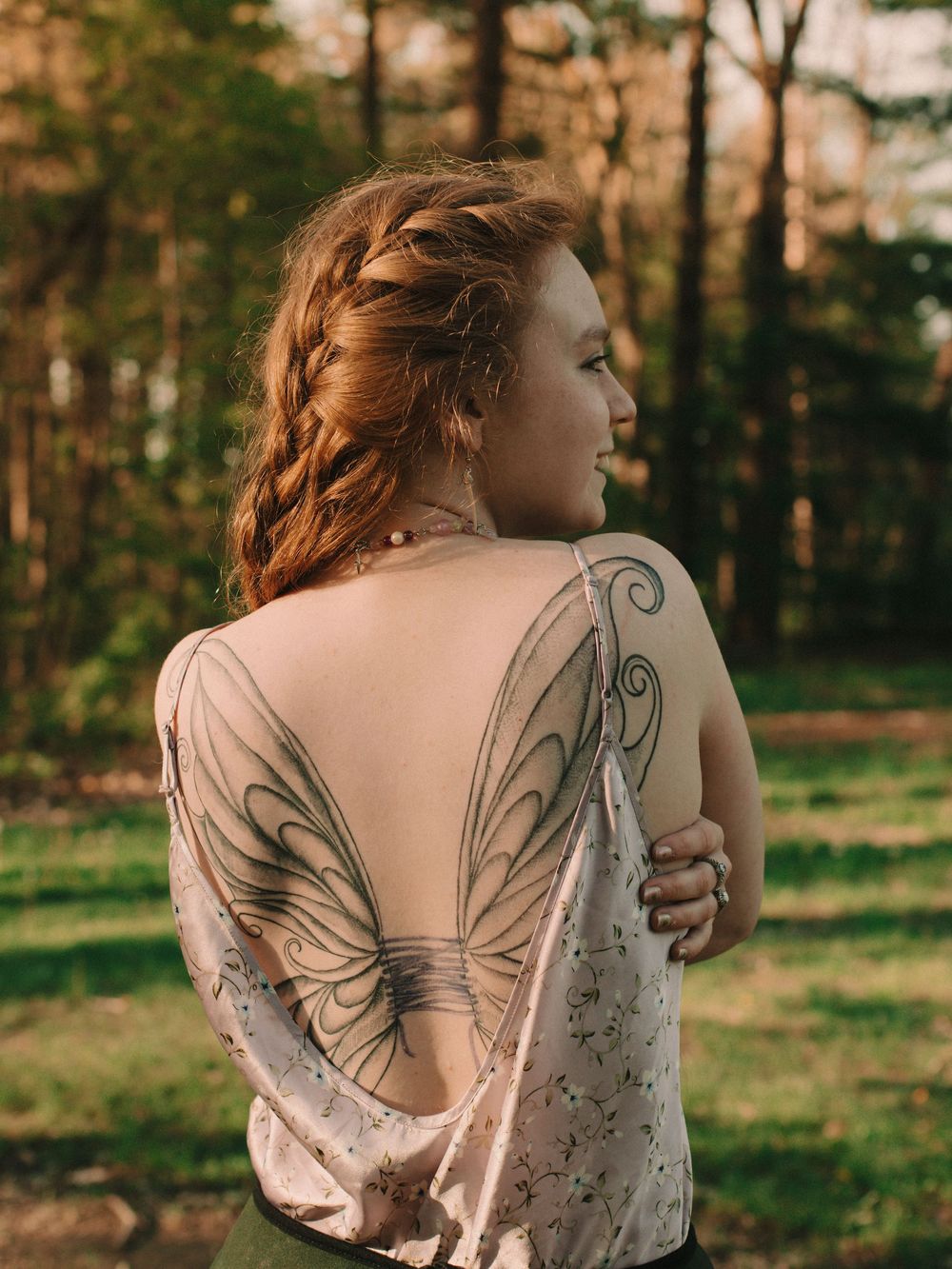 Woman with fairy wings tattoo in the woods during golden hour