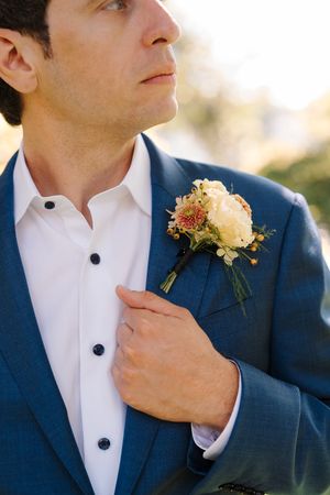 Close-up details of groom's boutonniere with yellow flowers pinned to navy blue suit jacket.