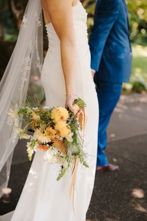 Elegant bridal bouquet with yellow flowers and greenery against white wedding dress.
