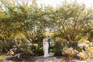 A couple shares a romantic moment in a garden setting with blooming trees and natural sunlight.