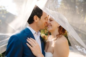 Romantic wedding couple shares intimate moments under flowing veil in soft natural light.