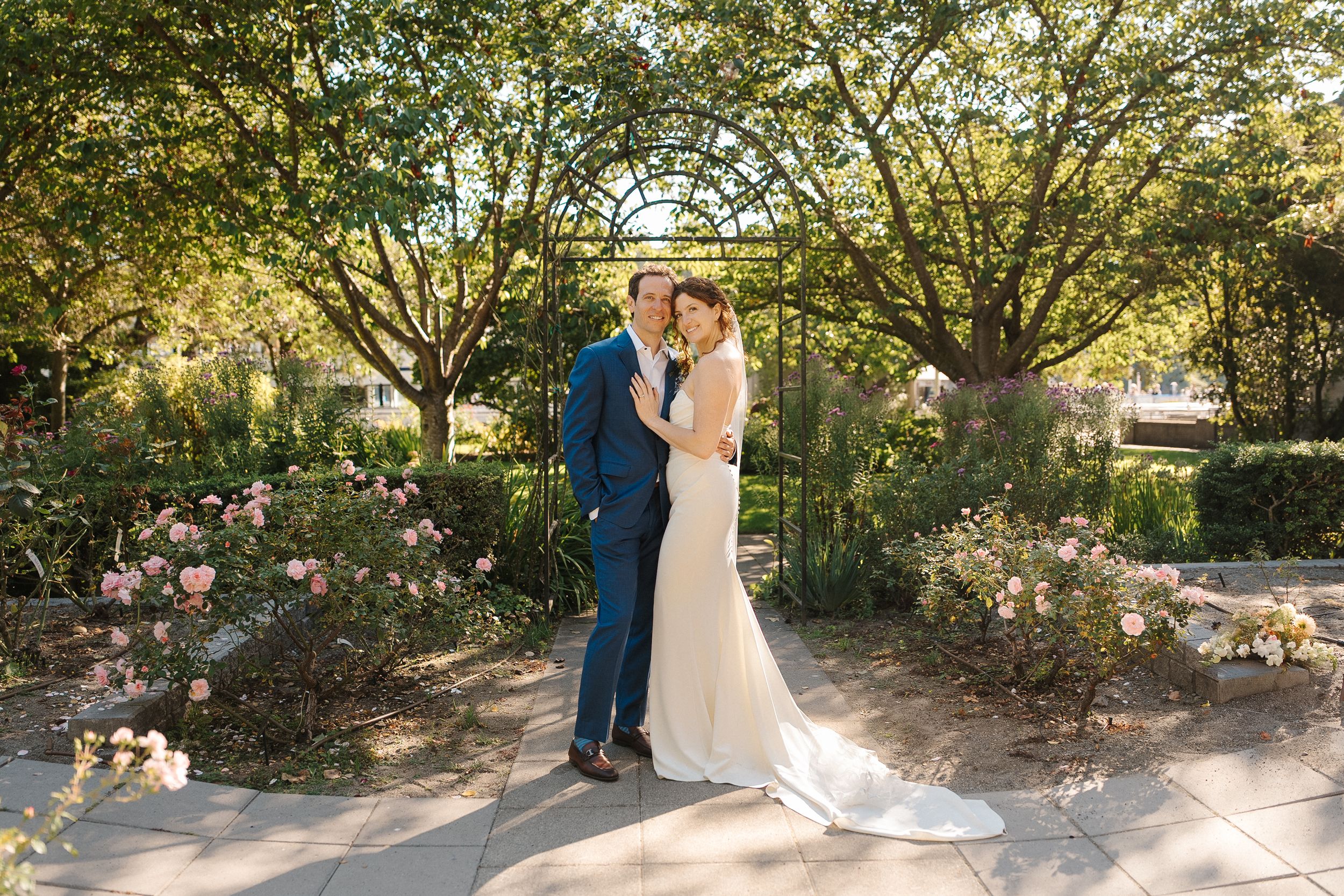 A couple shares a romantic moment under lush trees in a garden setting during their wedding celebration.