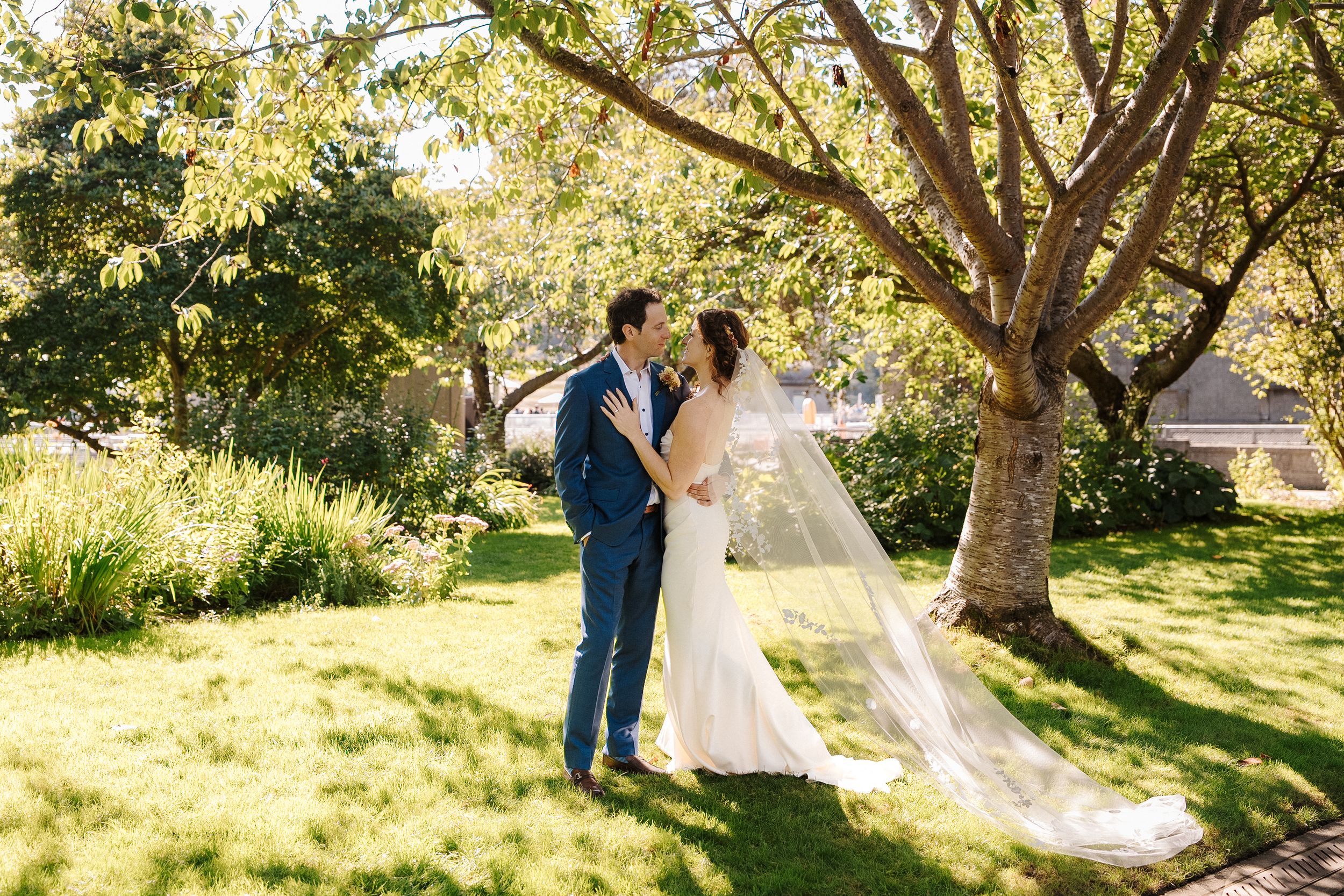 A couple shares romantic moments in a sun-dappled garden setting during their wedding photoshoot.