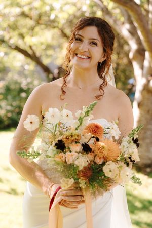 A bridal bouquet featuring soft peach and white flowers with delicate greenery captured in natural outdoor lighting.