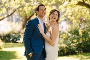 A couple shares joyful moments in a sun-dappled garden setting wearing formal wedding attire.