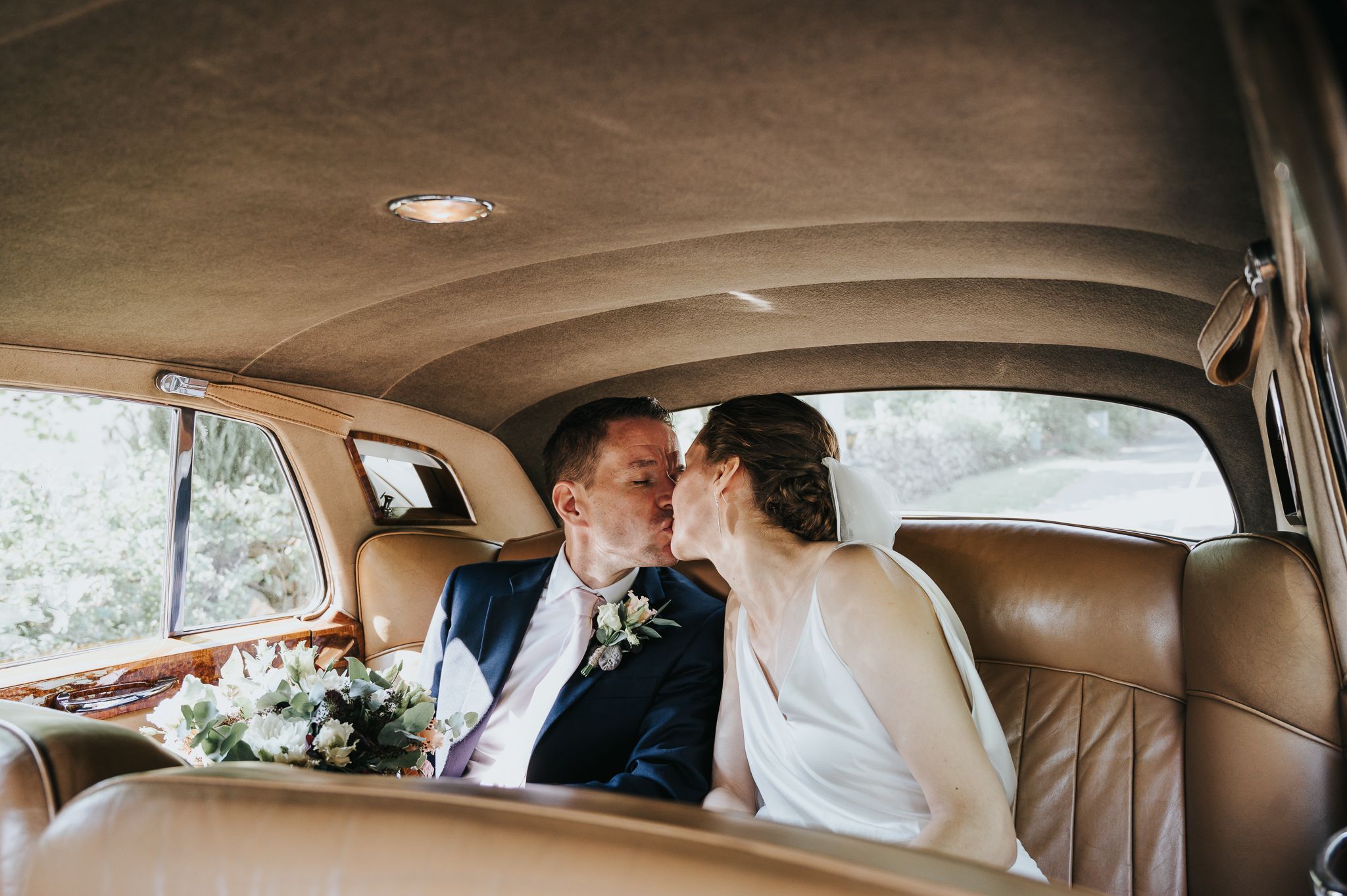 Romantic newlywed couple sharing intimate moment in classic car backseat.