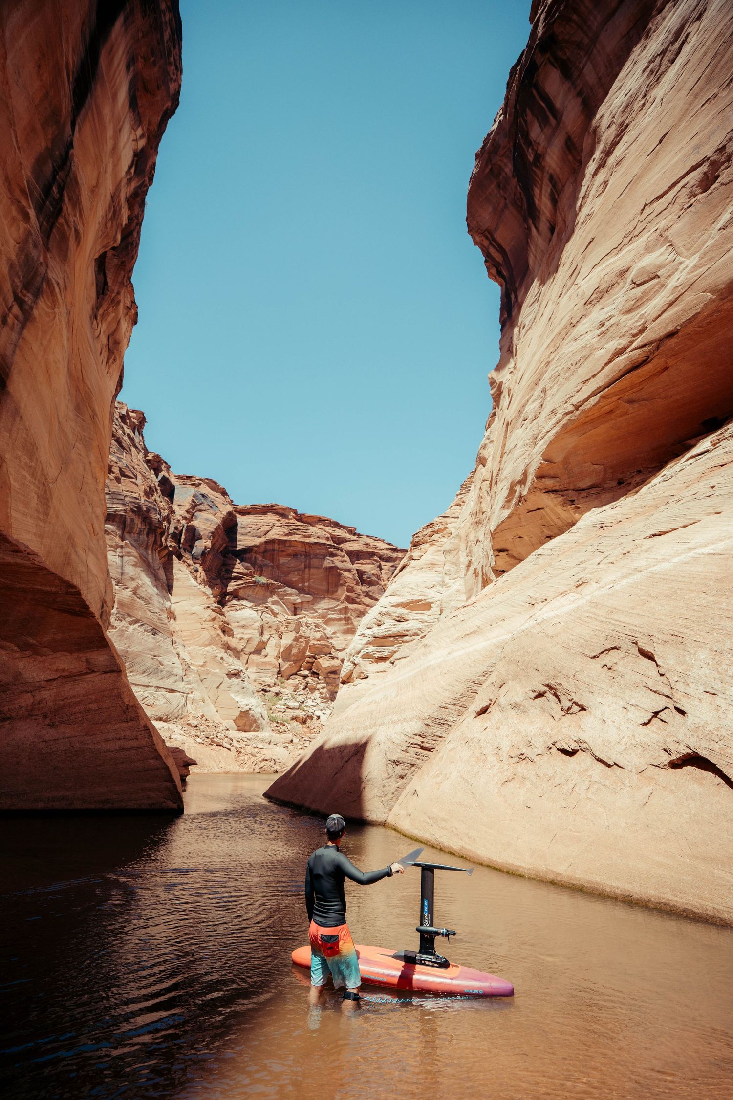 Kayakers paddle through narrow red rock canyons with towering sandstone walls reflecting in calm waters at Lake Powell.