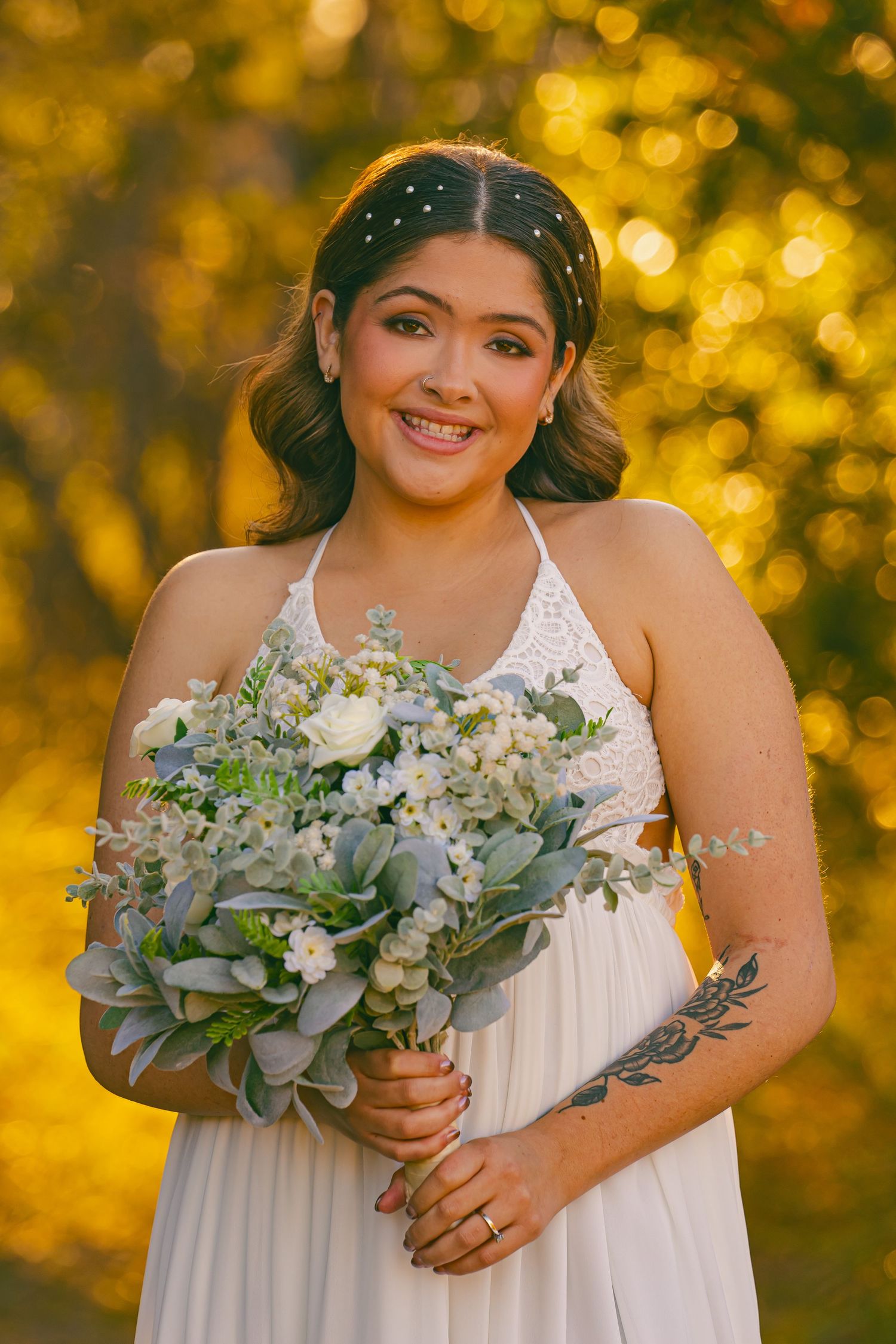 Wedding party members in casual attire form an arch over a couple walking beneath holding a blue-green bouquet.