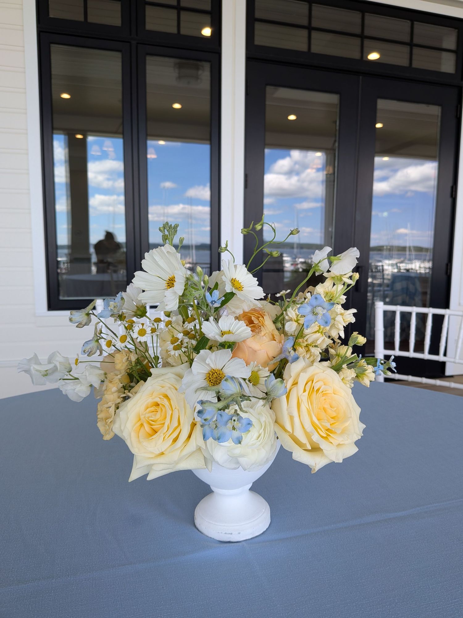 Elegant floral aisle decorations with peach roses and greenery line up alongside white wedding ceremony chairs outdoors.
