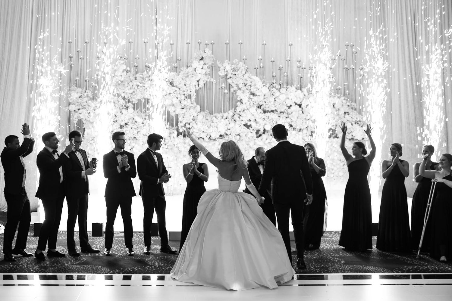 A black and white panoramic wedding photo showing a bridal party lined up against a bright window background.