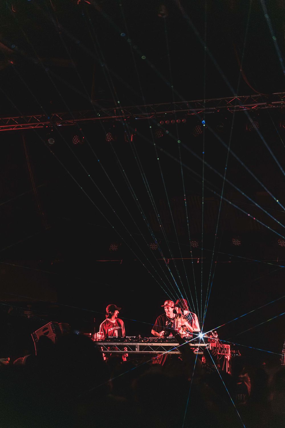 Silhouetted performers on stage with red lighting and laser beams creating dramatic atmosphere at an electronic music show.