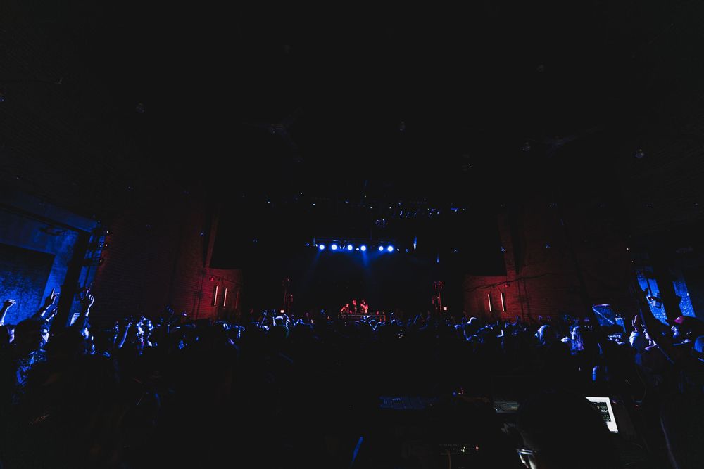 Concert crowd silhouettes against a dark stage illuminated by blue and red lights during a live performance.