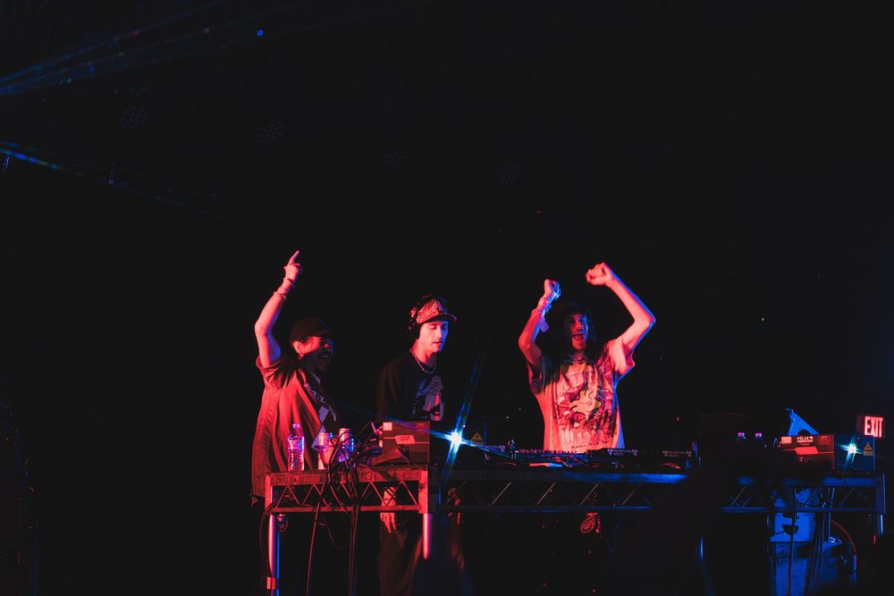 DJs perform on stage with raised hands under dramatic red and blue lighting during a nighttime concert performance.