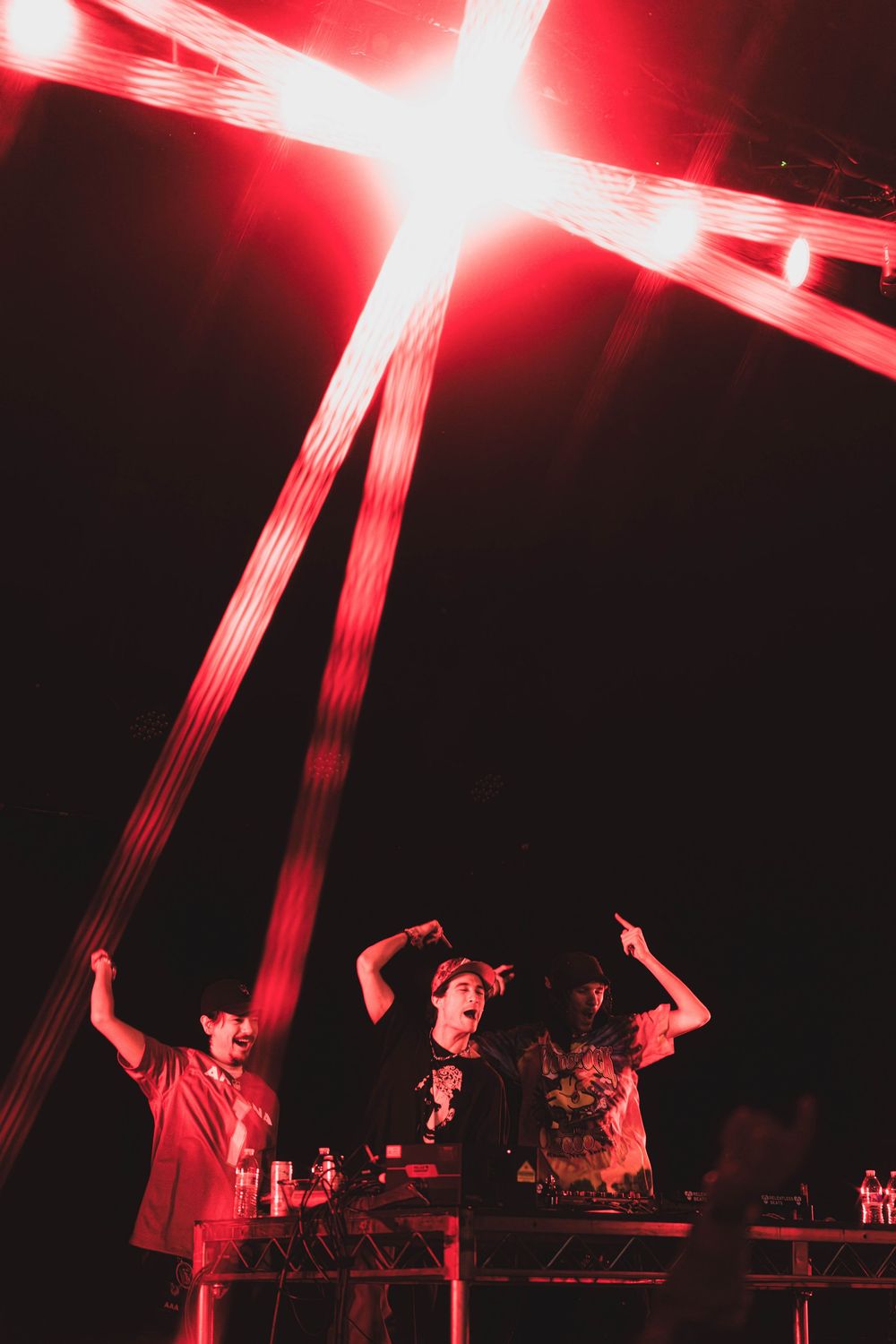 DJs perform on stage under dramatic red lighting at an electronic music event.