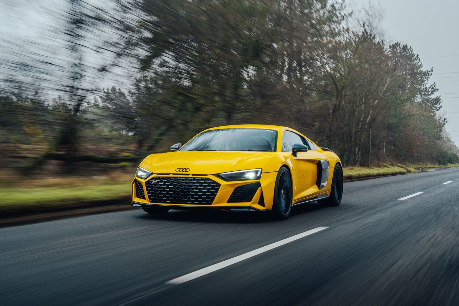 Yellow Audi R8 sports car driving on a winding road through autumn scenery.