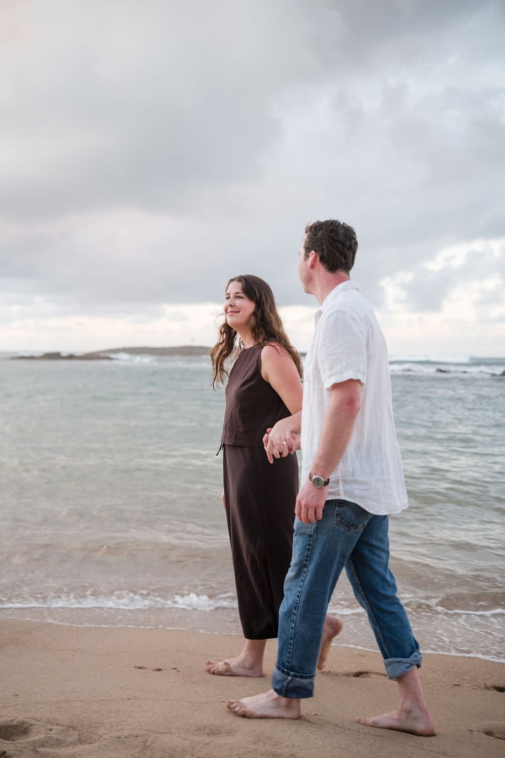 Couple standing near ocean during engagement session with waves in background