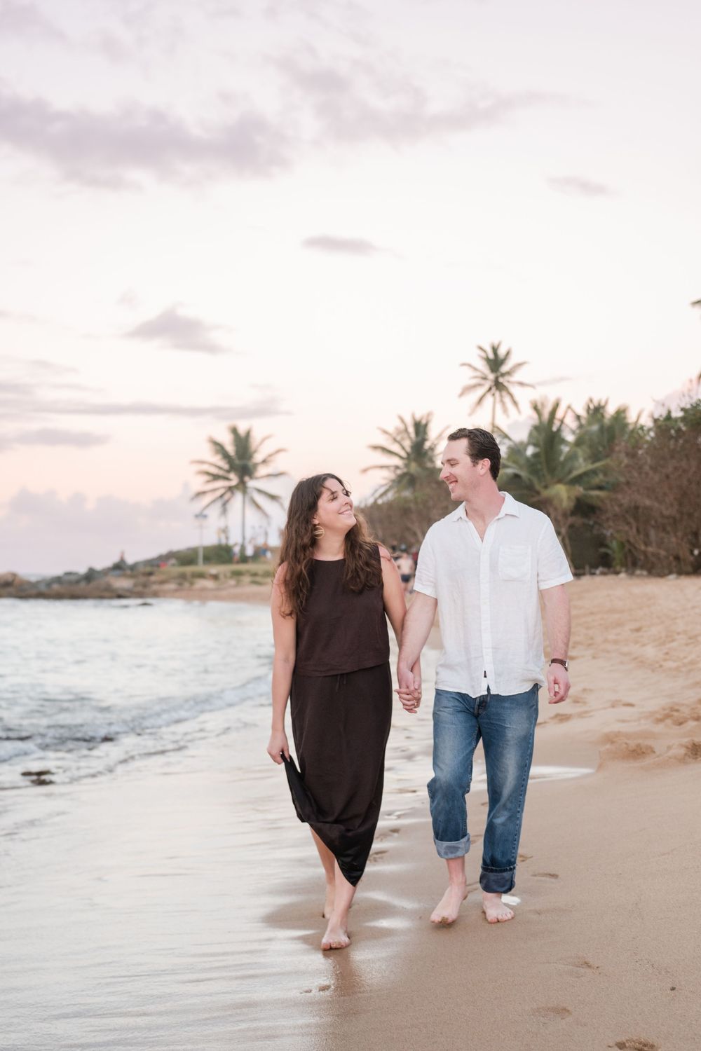 Couple walking together along beach during golden hour engagement session