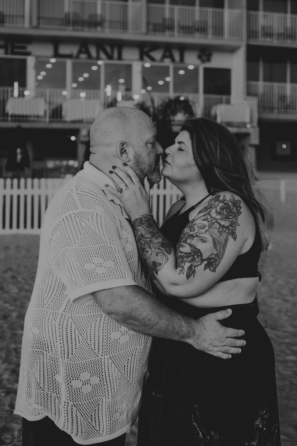 A romantic couple embraces and kisses on the beach in a black and white photo series.