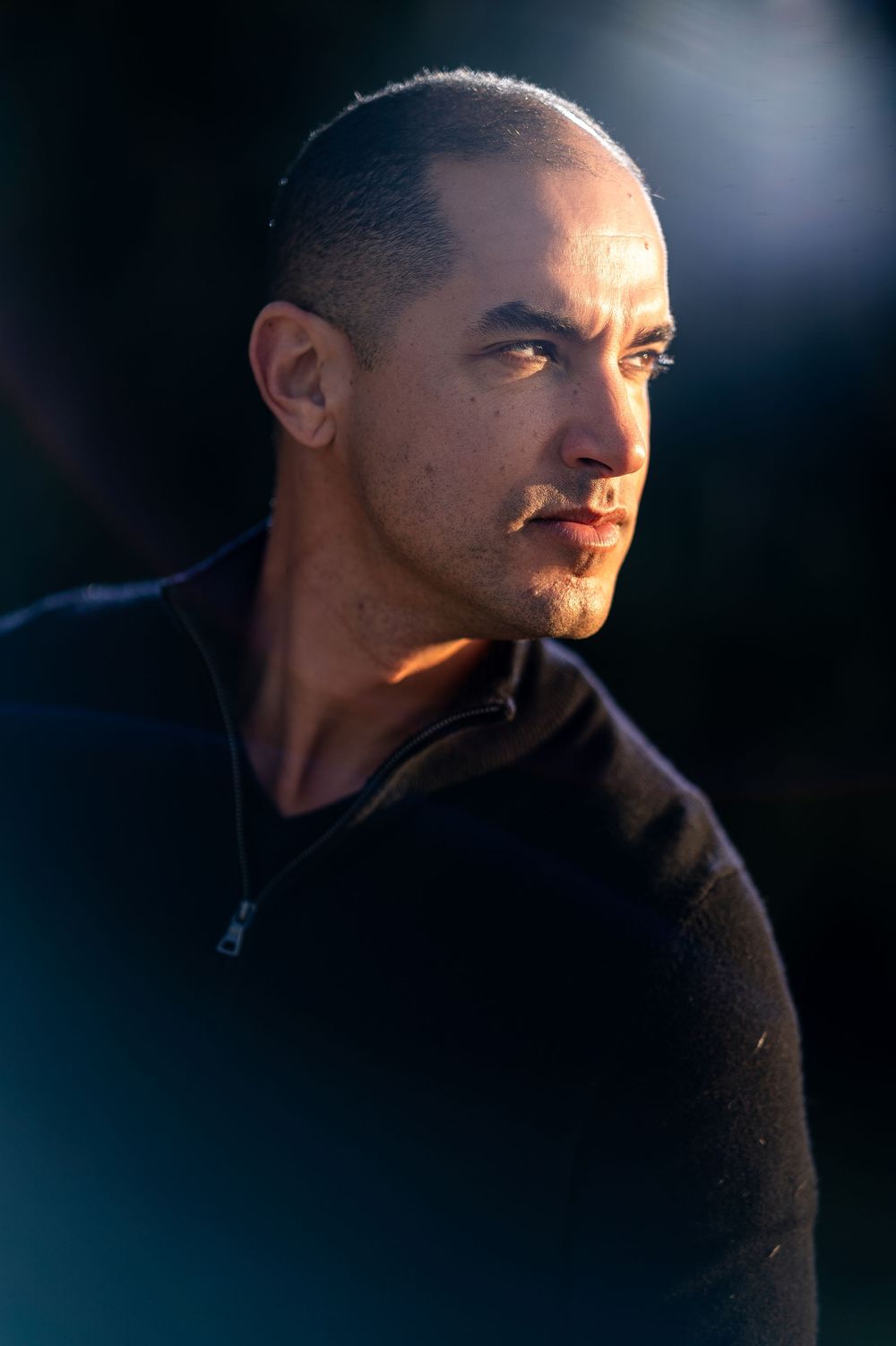 Profile view of someone wearing a dark sweater against a dark background with dramatic lighting.