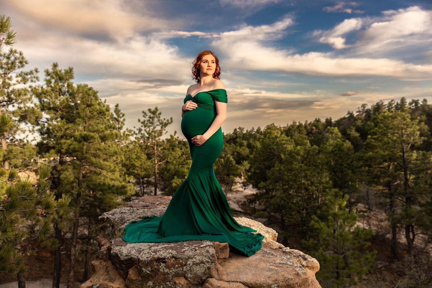 A person in an emerald green dress poses gracefully against a dramatic sunset sky and rocky mountain backdrop. Palmer Park, Colorado Springs