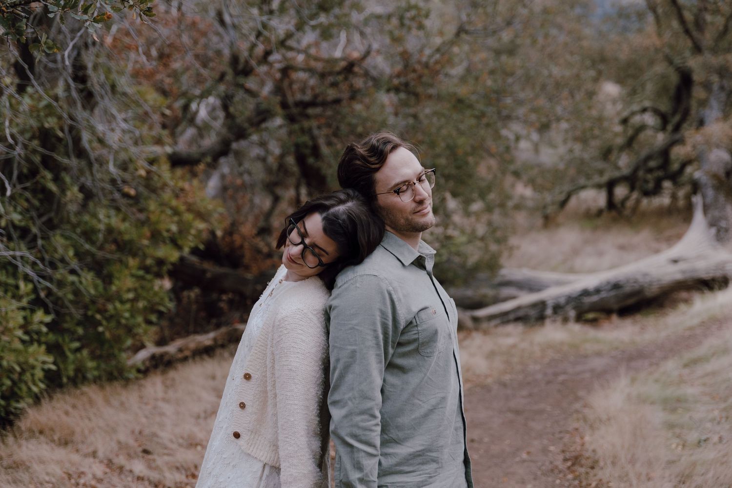 A couple walks together through a scenic wooded path during an autumn engagement photoshoot.