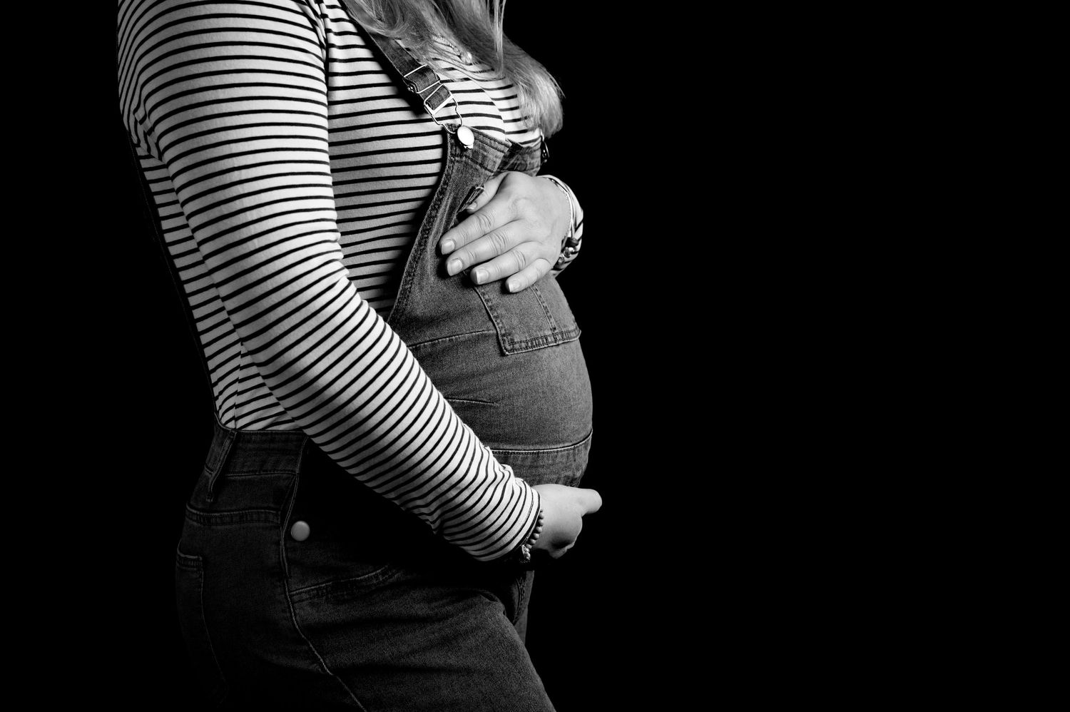 A series of black and white maternity photos showing a pregnant belly in a striped shirt against dark backgrounds.