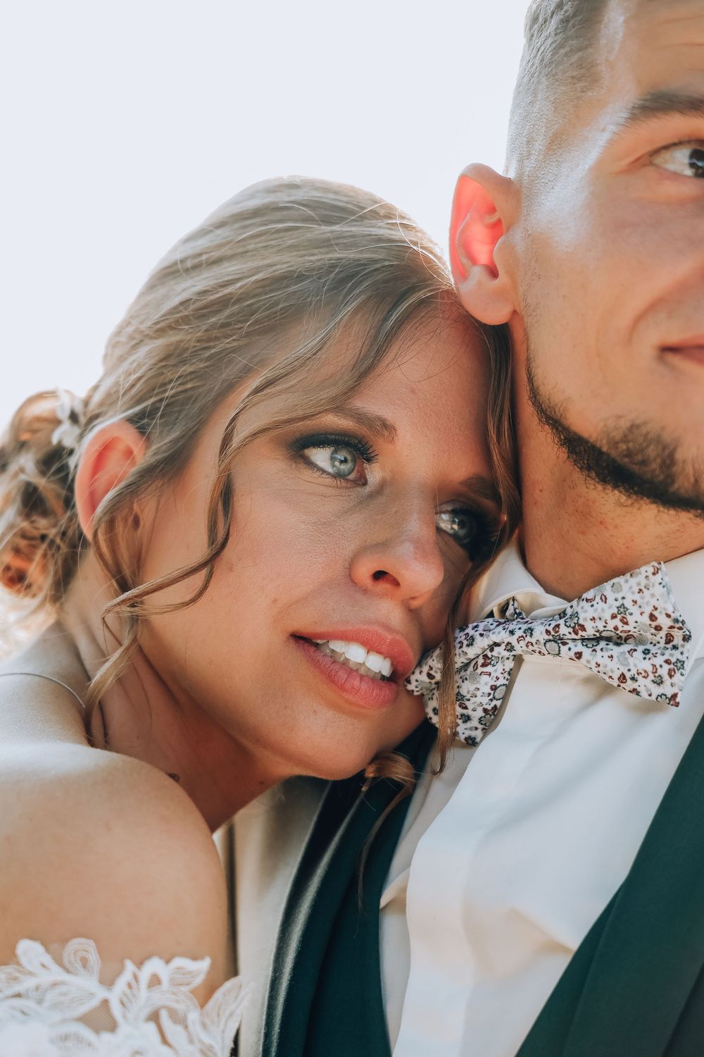 Close-up portrait of bride leaning on grooms shoulder, showcasing her blue eyes and his floral bow tie.