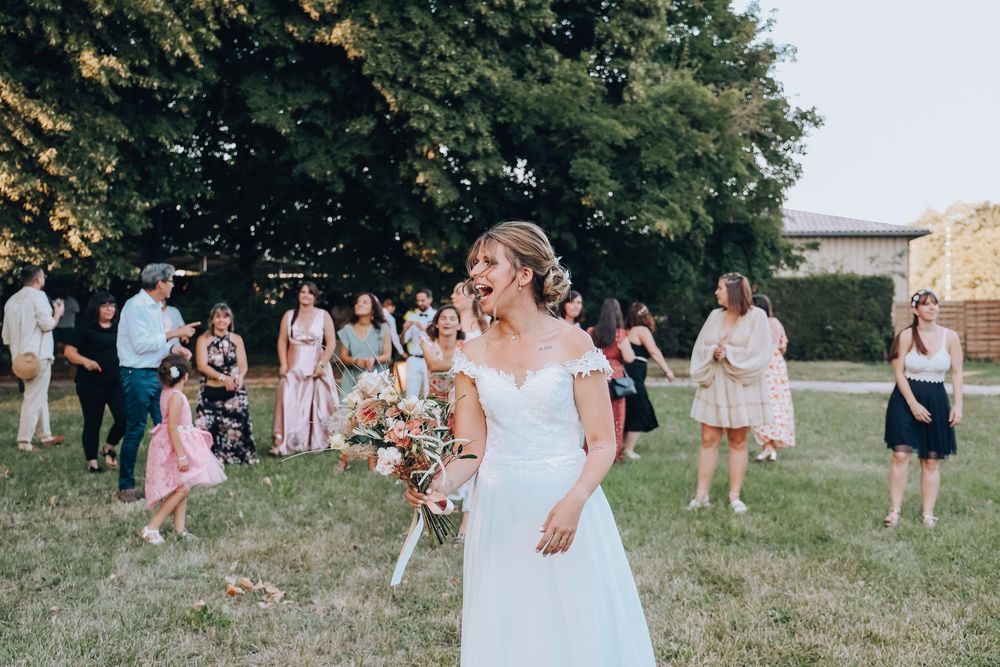 Joyful bride in white gown tossing bouquet surrounded by cheering wedding guests outdoors.