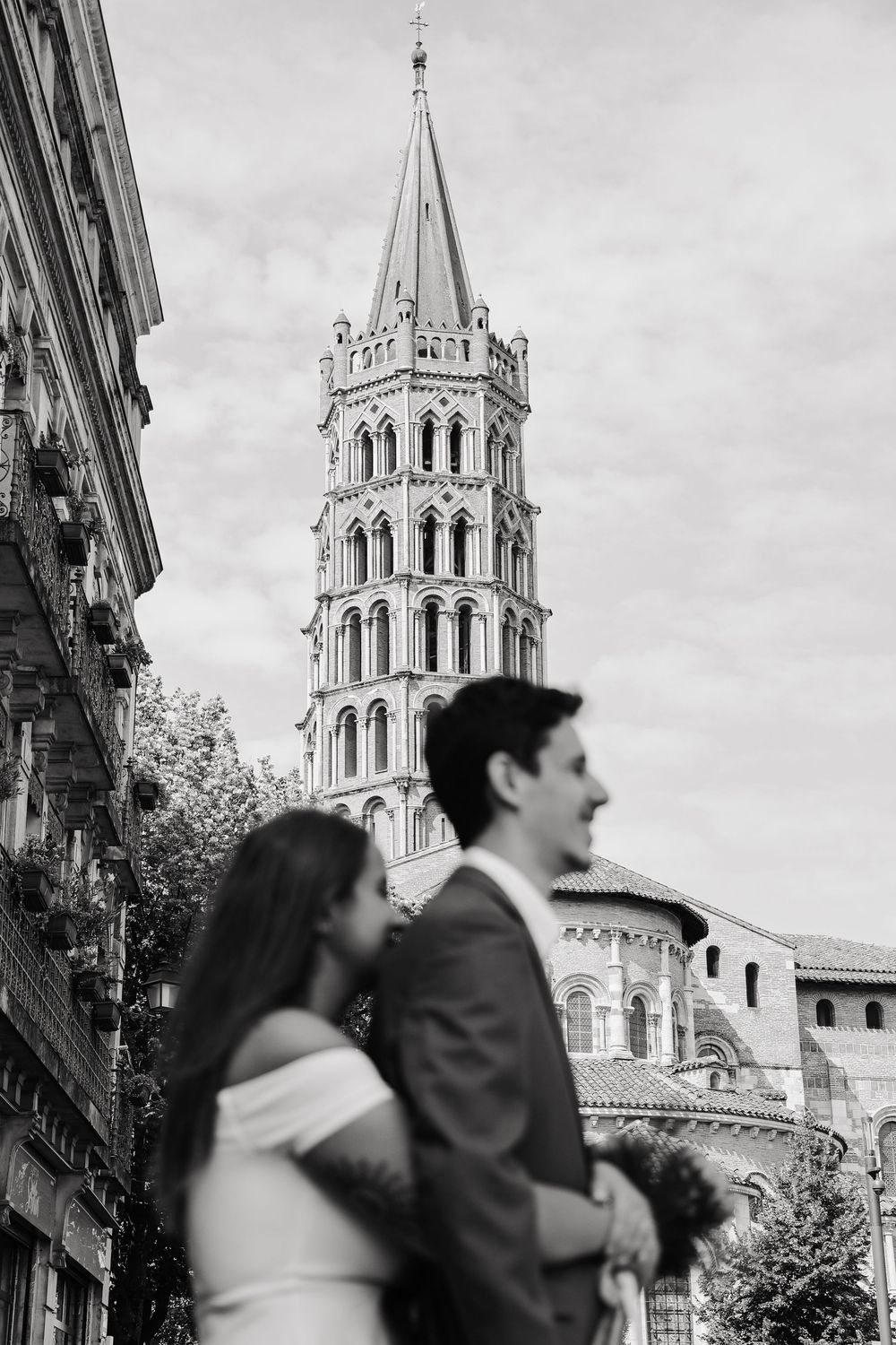 Black and white photo of wedding couple standing together with the ornate Saint-Sernin tower behind them.