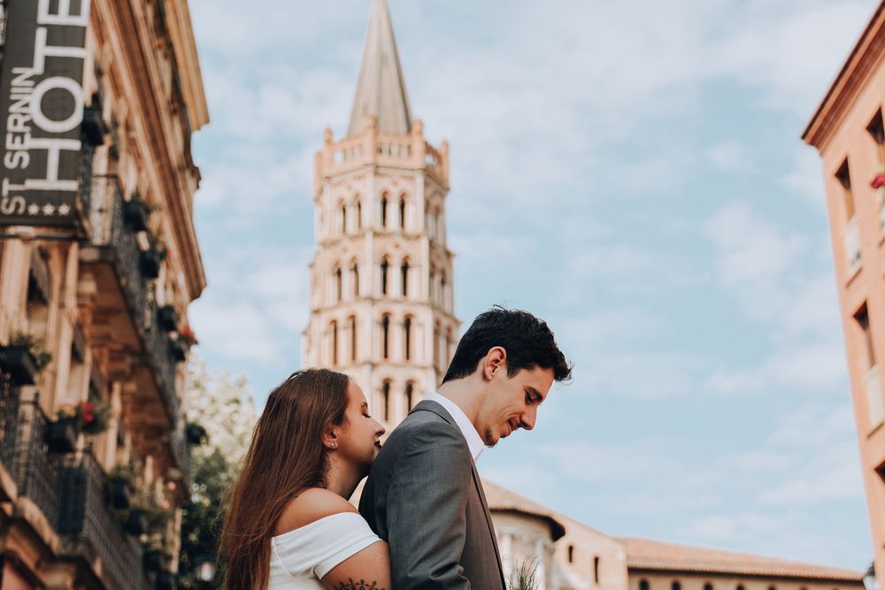 Bride and groom gazing at each other with the Saint-Sernin Basilica bell tower rising behind them.
