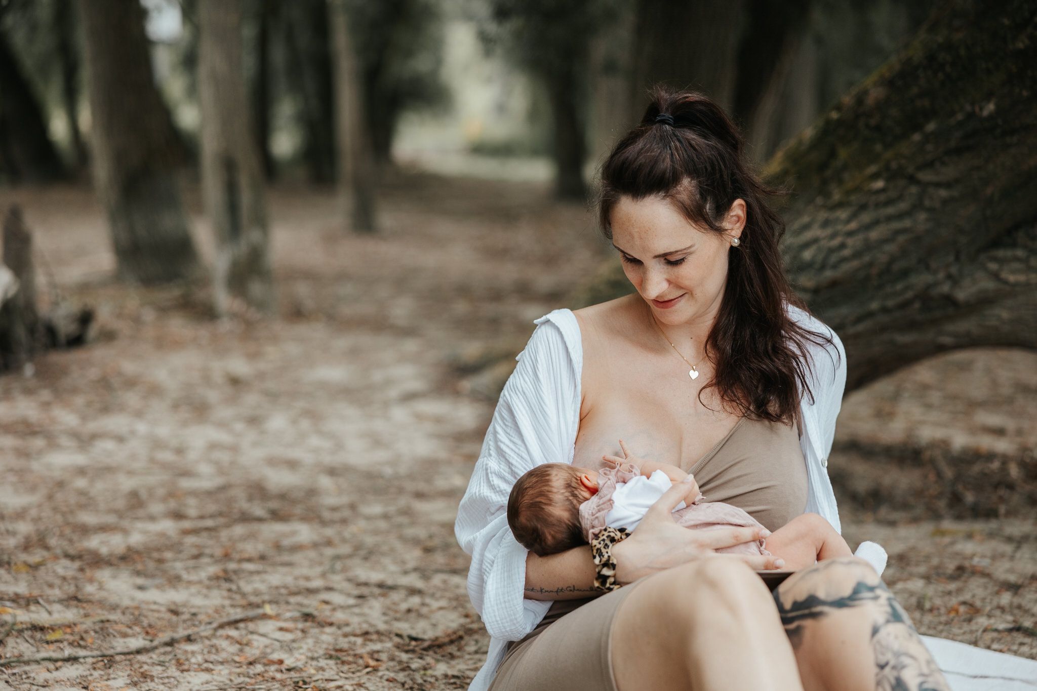 Mother nursing newborn baby in a peaceful outdoor forest setting with soft natural lighting.