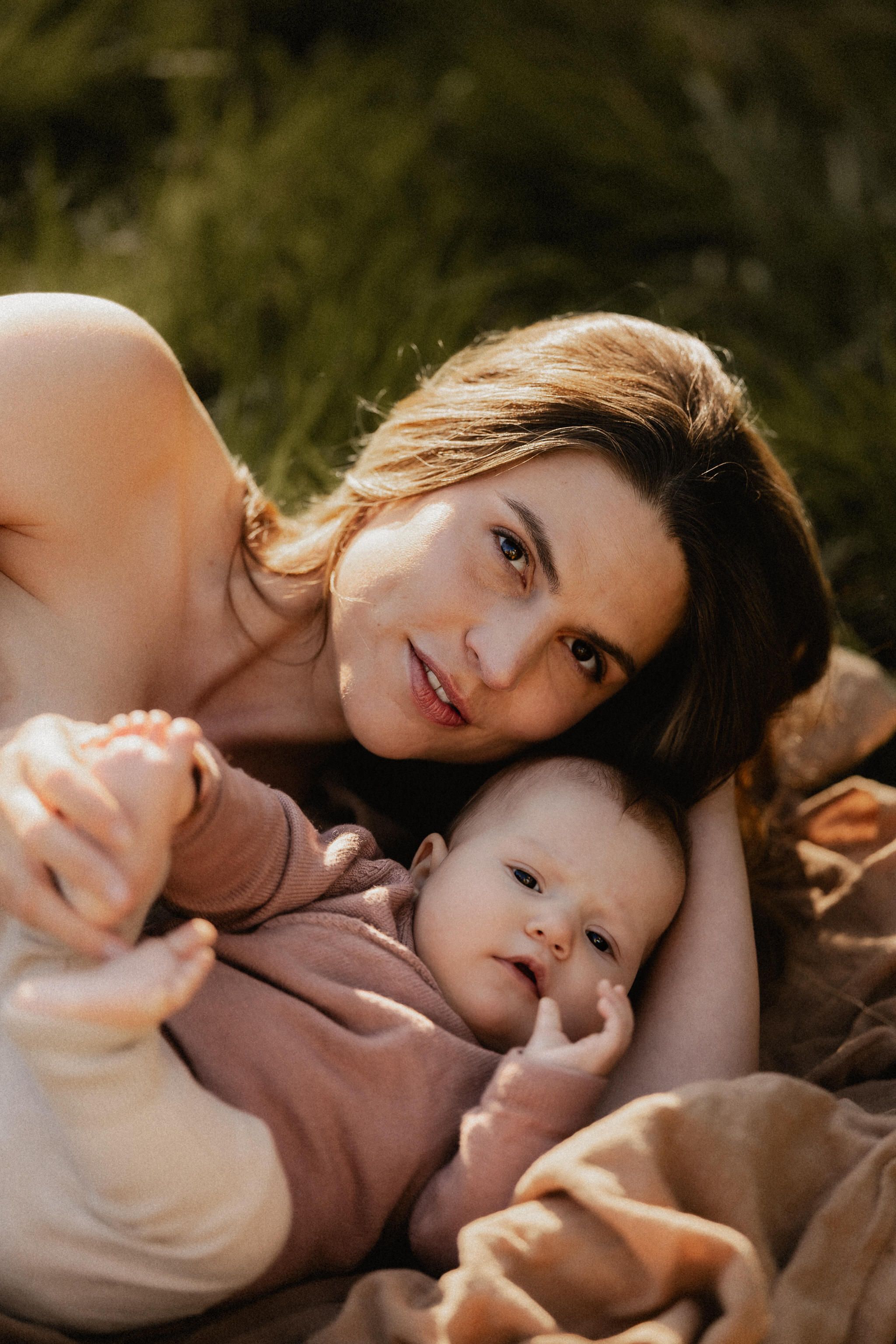 A parent and child lie together on grass in warm sunlight, sharing tender moments across multiple candid poses.