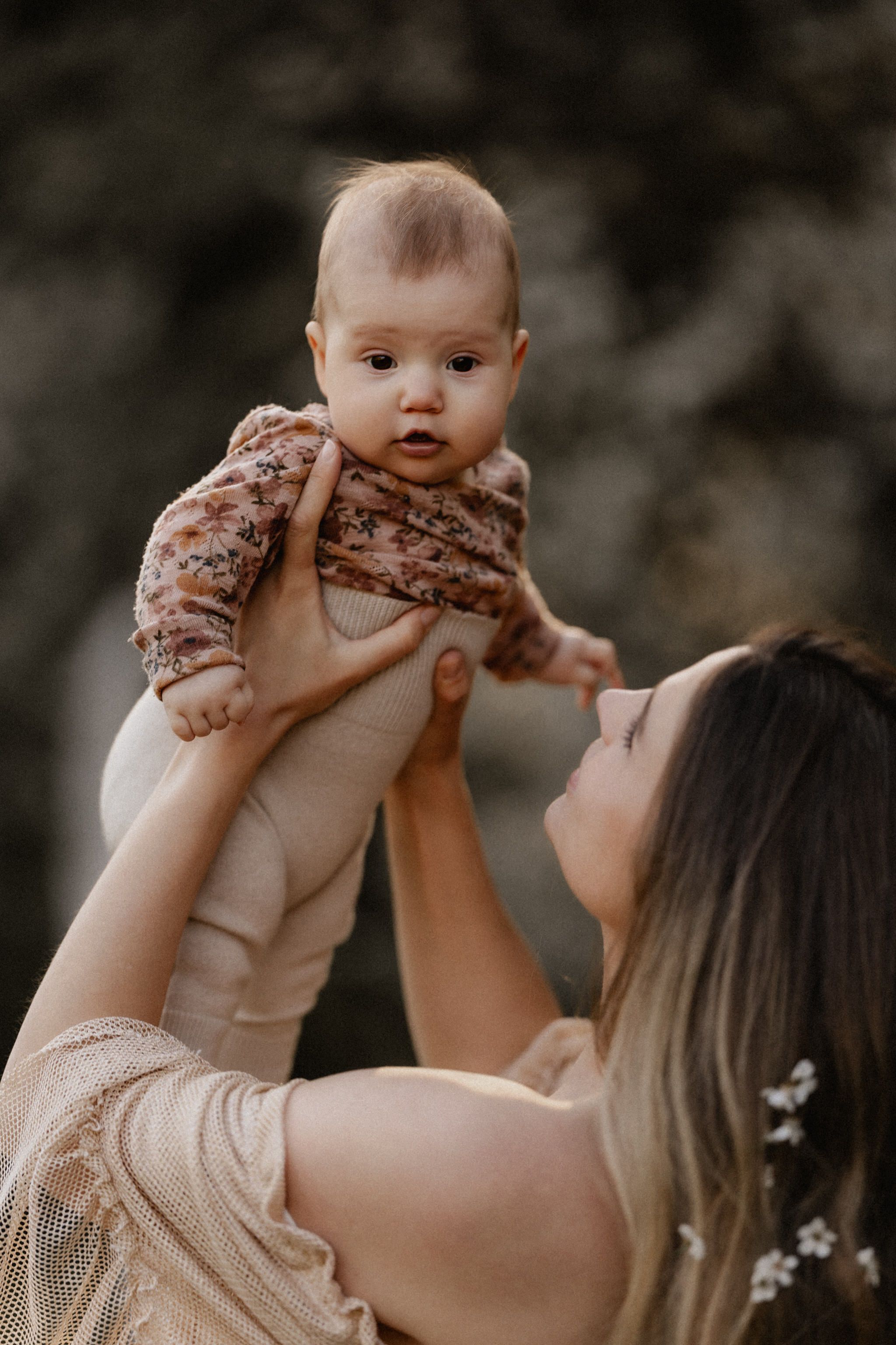 A parent lifts a baby wearing a beige outfit in a series of connected outdoor portrait photos.