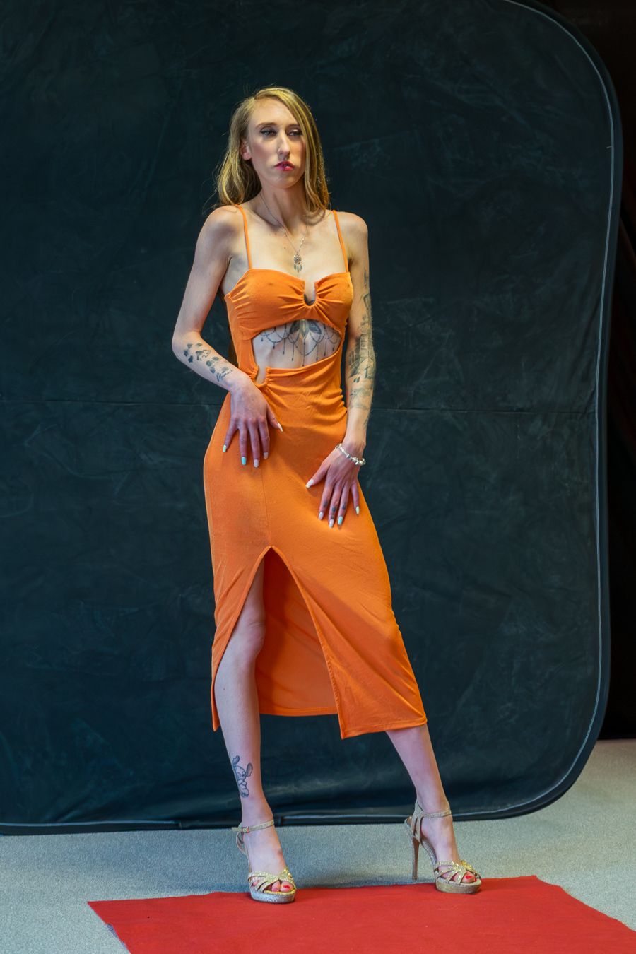 Model wearing orange sundress strikes dynamic poses during fashion photoshoot on red carpet.