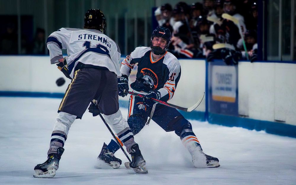 Two hockey players battle for the puck along the boards, both focused and determined by SportsFox Photography, Hershey,