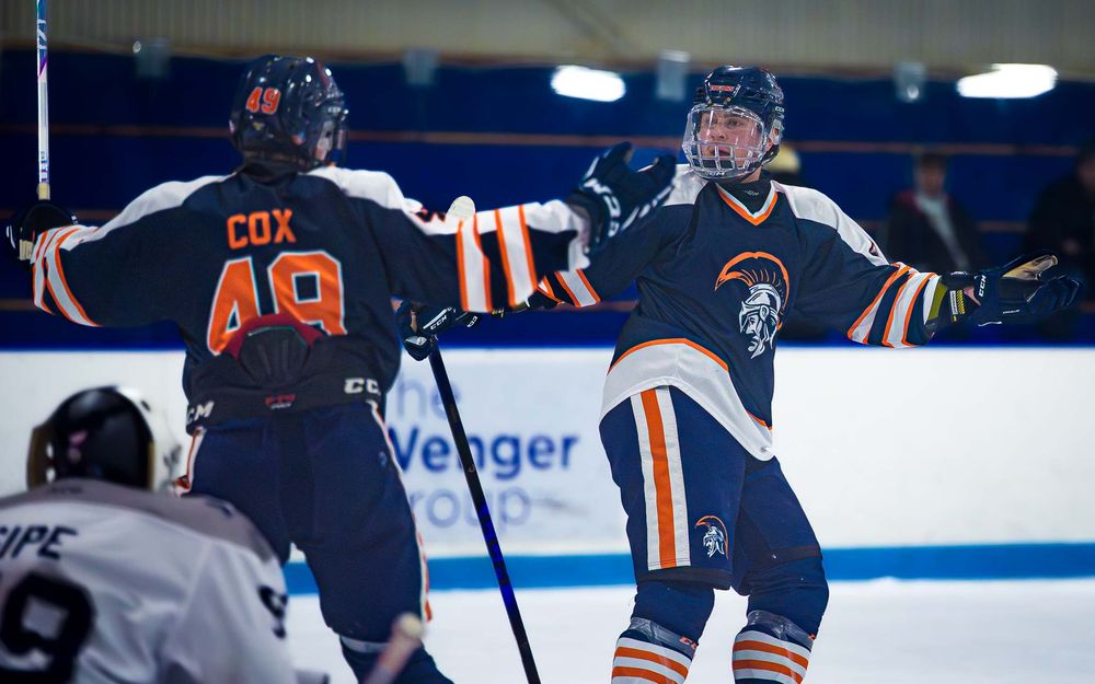 Trojans teammates celebrate a goal with arms raised in front of the boards by SportsFox Photography, Hershey,