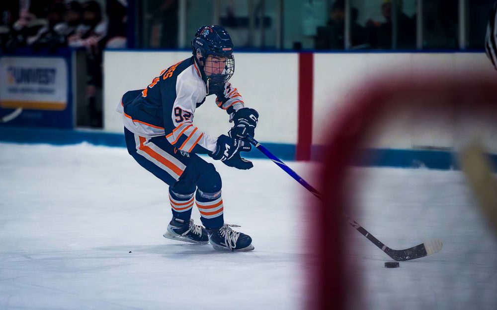 Trojans forward skates behind the net, puck on stick, with the red goalpost visible in the foreground by SportsFox Photography, Hershey,