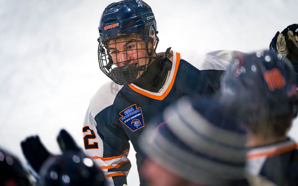 Close-up of a Trojans player’s face behind a helmet, celebrating a goal skating by the bench by SportsFox Photography, Hershey,