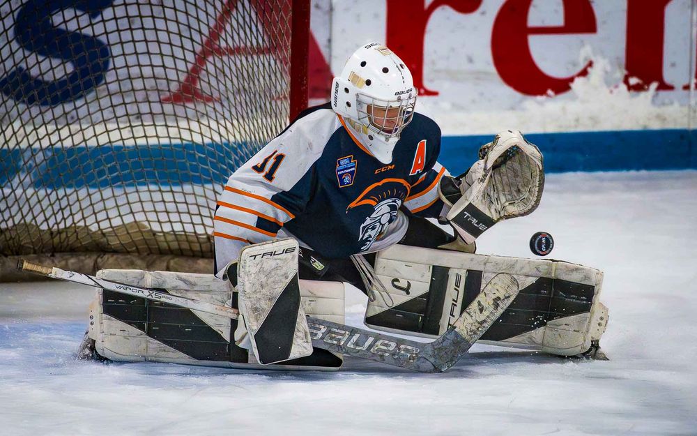 Trojans goalie stretches out to block a low shot with pads, eyes on the puck by SportsFox Photography, Hershey, PA