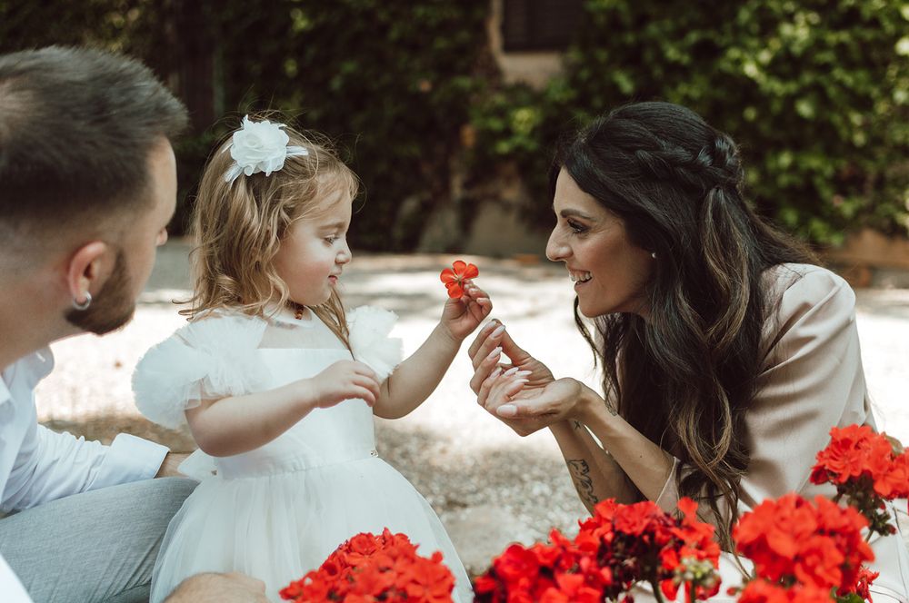 momento di fotografie di famiglia durante in battesimo della loro bambina, la bambina porge un fiore rosso alla mamma.