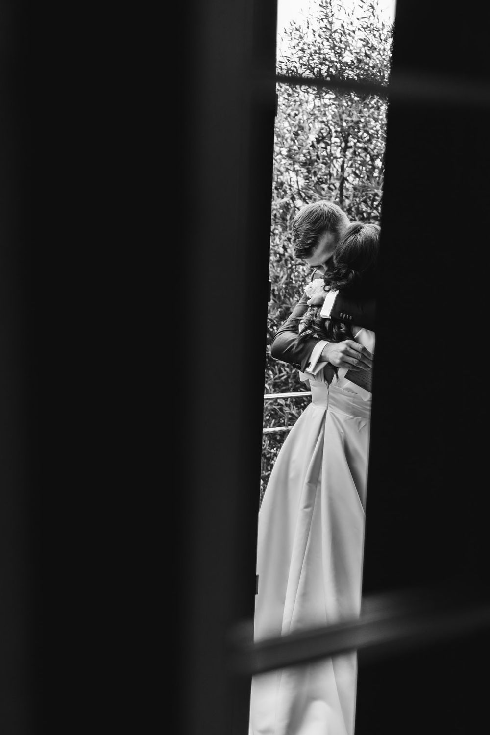 Fotografia artistica in bianco e nero di un attimo rubato di sposi attraverso le colonne delle finestre.