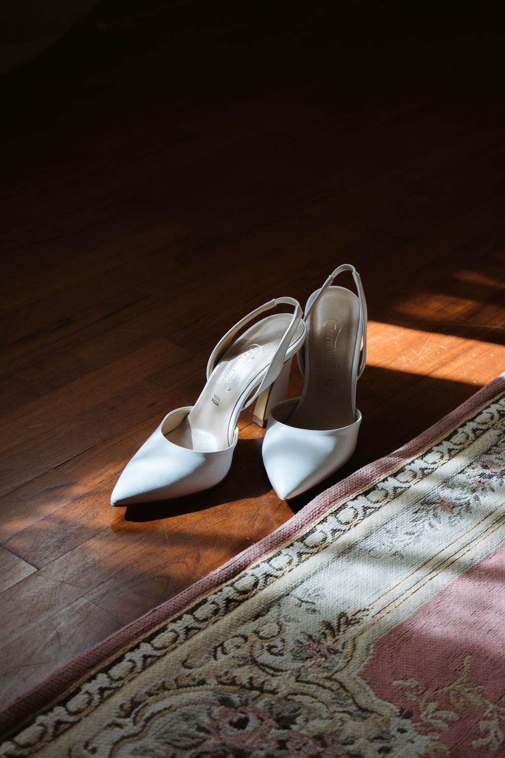 Eleganti scarpe da sposa bianche su un tappeto tradizionale con un'illuminazione drammatica.