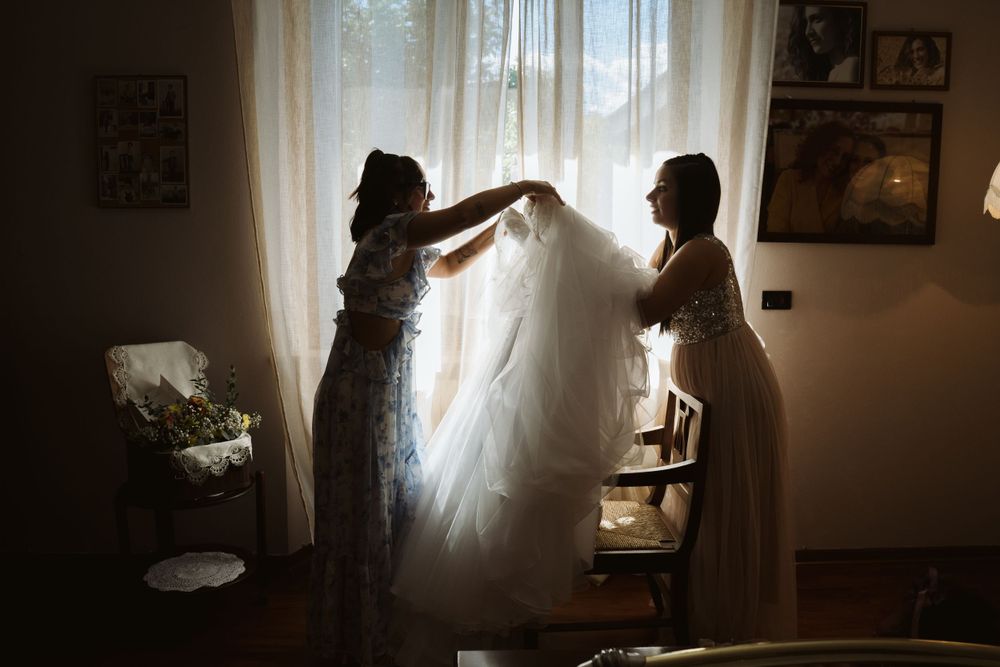 Vestizione della sposa, in maniera elegante, controluce, spontanea. la sposa che cerca di uscire dall'abito con le sue damigelle.