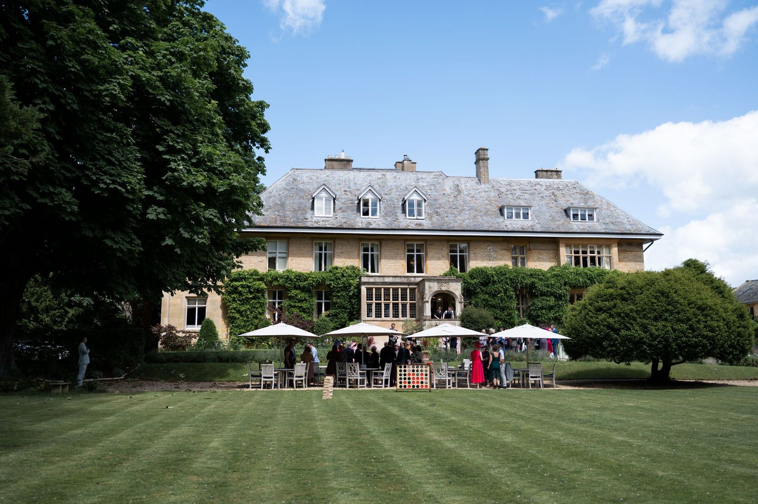 Elegant manor house wedding venue with guests gathered on manicured lawn under white parasols.