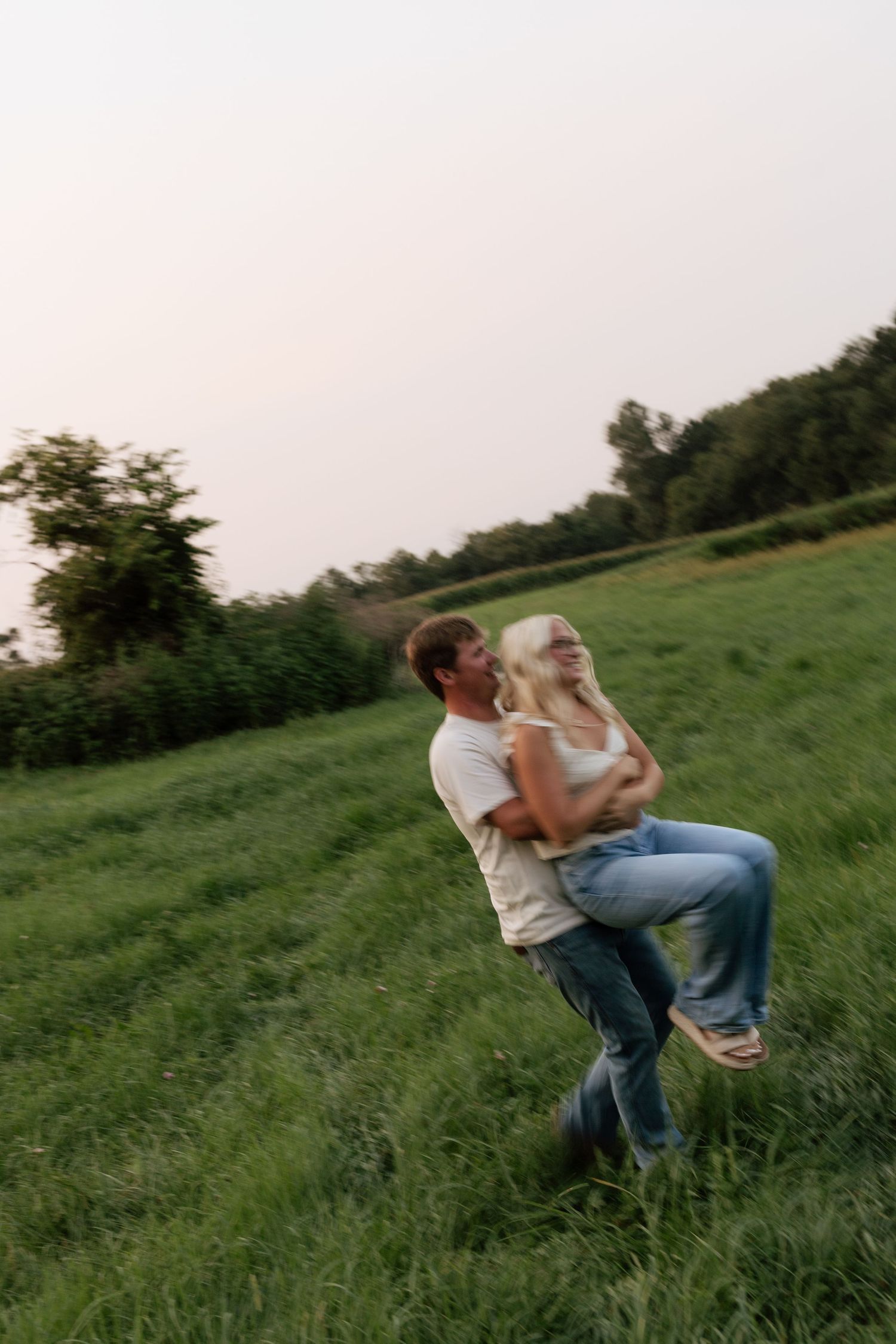Romantic couple kissing by a chain-link fence railing at an outdoor sports facility on a cloudy day.