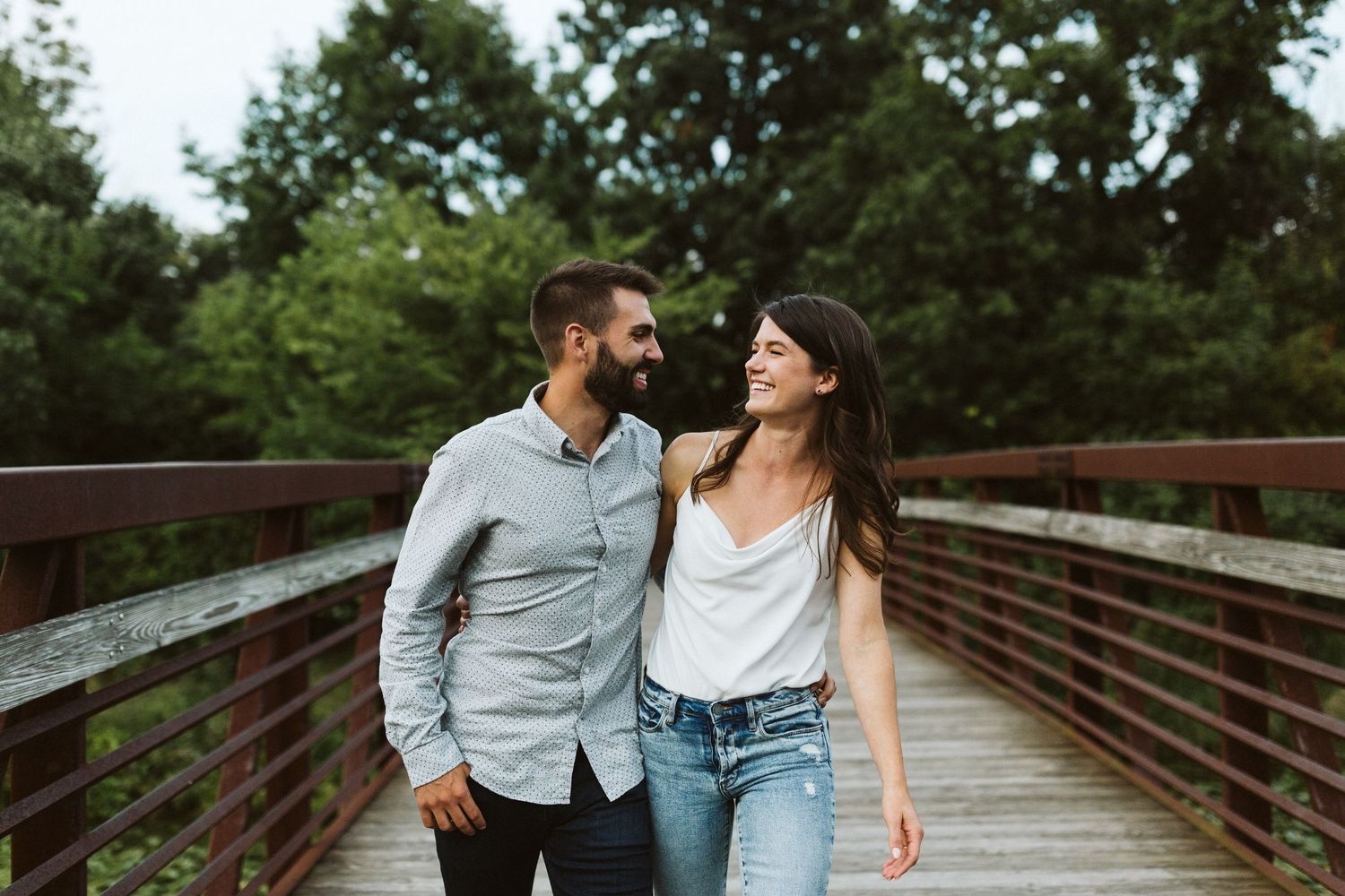 A couple shares romantic moments on a wooden bridge surrounded by lush greenery on a summer day.
