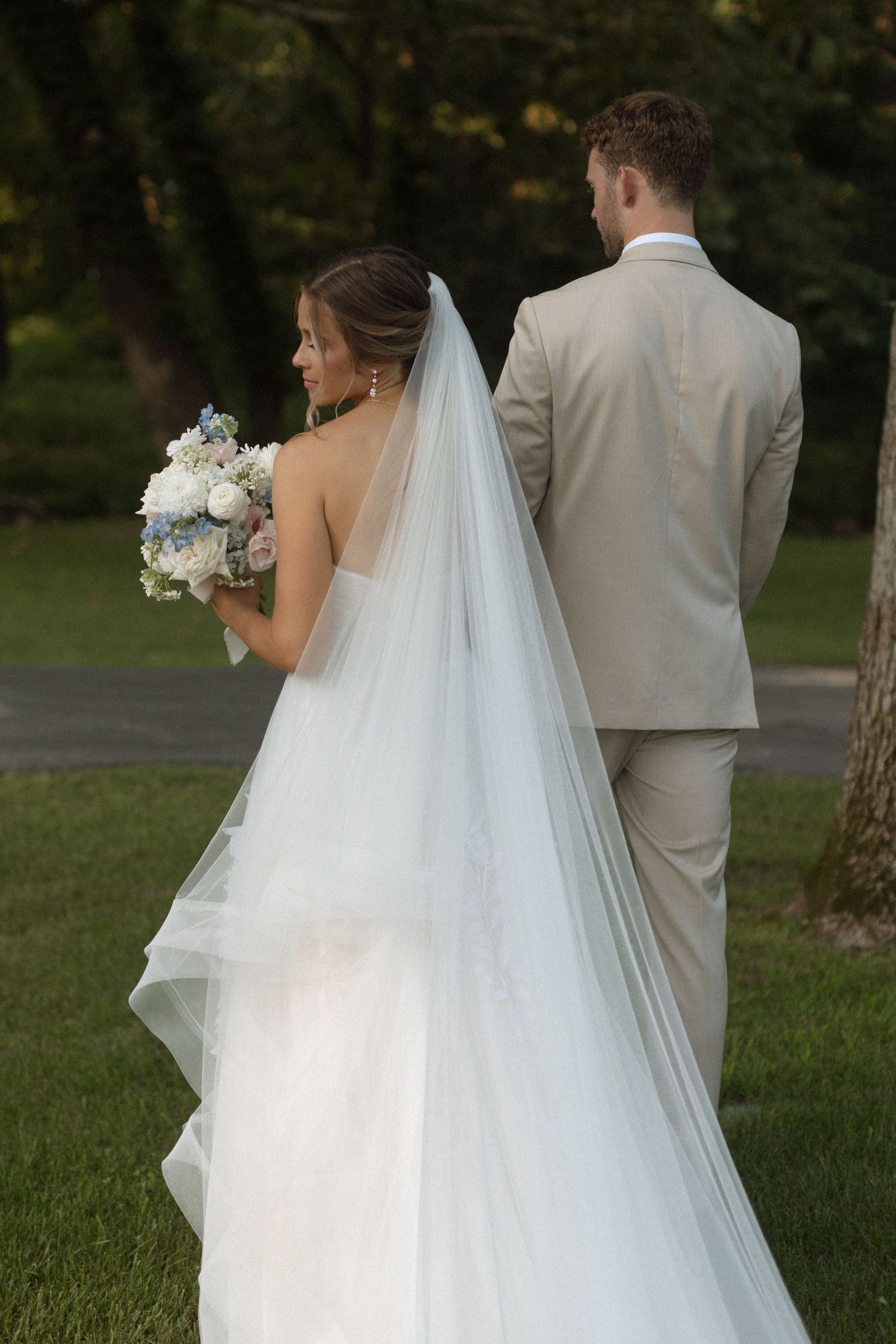 Wedding party walks together under olive trees at sunset while bride lifts her white dress.