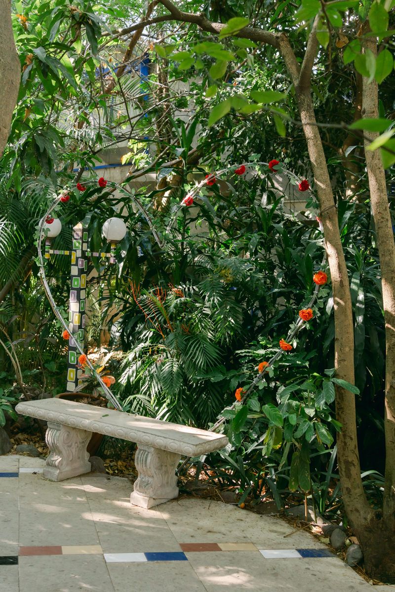 Stone benches line a lush garden path decorated with hanging red flowers and tropical greenery.