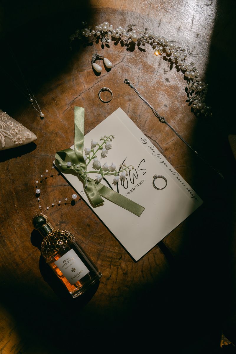 Wedding invitation and decorative elements arranged on a dark wooden surface in moody lighting.