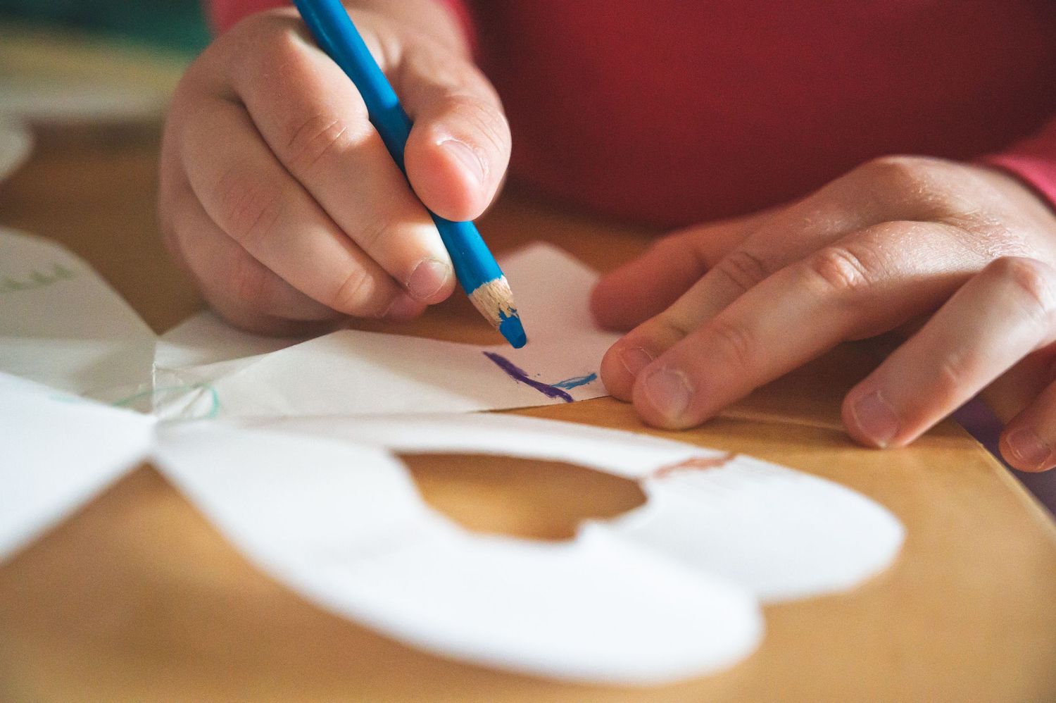 Close-up view of hands holding a blue pencil while drawing or tracing on white paper.